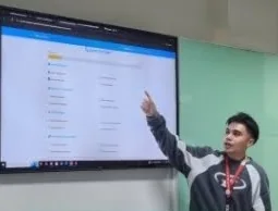 A student pointing at a list view on a wall screen while presenting to the room.